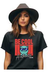 Femeie purtând un tricou negru cu designul 'Be Cool Authentic' și o ilustrație colorată a unei pisici cu ochelari de soare albastri, completat de o pălărie elegantă.