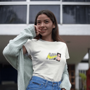 Femeie purtând un tricou alb cu un design grafic ce include textul 'NIKE' și un personaj stilizat(Catwoman), având pe umeri un cardigan deschis și pozând afară, zâmbind ușor.