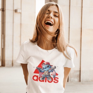 Fată zâmbitoare purtând un tricou alb cu un design grafic colorat ce înfățișează un personaj animat stilizat(Stitch) și un logo creativ în roșu, într-un cadru luminos și deschis.