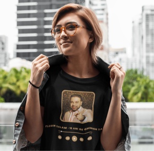 Femeie cu păr scurt și ochelari, purtând un tricou negru cu un design ce îl prezintă pe Florin Salam, alături de textul 'Florin Salam - 10 ani de ghinion salam'. Imaginea este încadrată într-un stil de player muzical, cu butoane de control vizibile în par