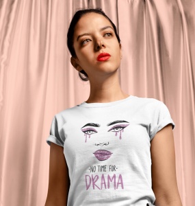 Fată cu expresie serioasă, purtând un tricou alb cu un design grafic ce afișează un portret stilizat de femeie cu machiaj dramatic și textul 'No time for drama', pe un fundal de draperii roz.