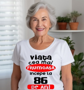 Femeie care poartă un tricou alb personalizat cu mesajul: ''Viata cea mai frumoasa incepe la 86 de ani''.