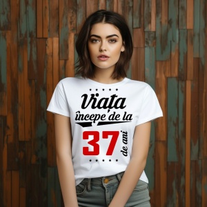 O femeie purtând un tricou alb cu textul  'Viața începe de la 37 de ani'. Fundal din lemn cu diferite nuanțe de maro și verde.