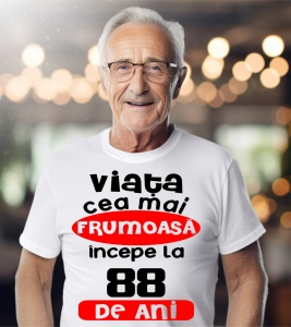 Un bărbat purtând un tricou alb cu textul ''Viața cea mai frumoasă începe la 88 de ani''.