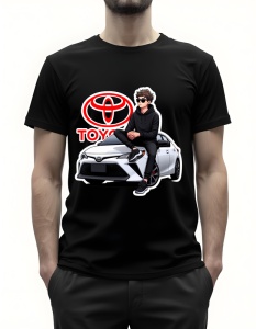 Bărbat purtând un tricou negru cu un design grafic reprezentând un tânăr așezat pe capota unei mașini Toyota albă, purtând ochelari de soare și o ținută casual, cu logo-ul Toyota afișat deasupra.