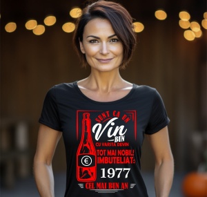 Femeie zâmbitoare purtând un tricou negru cu un mesaj în română despre vin, în care se menționează că este ca un vin bun care devine mai nobil cu vârsta, îmbuteliat în 1977, cel mai bun an.