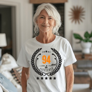 Femeie zâmbitoare purtând un tricou personalizat cu mesajul: ''94 ani de excelenta''