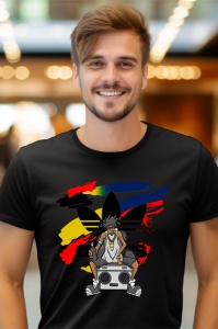 Bărbat cu zâmbet larg, purtând un tricou negru cu un design artistic ce include logo-ul Adidas și o imagine stilizată a unei persoane cu pălărie mare, stând pe o ladă de difuzor, în fața unui fundal luminos dintr-un spațiu interior.