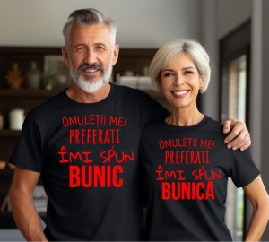 Un cuplu în vârstă purtând tricouri negre personalizate cu text roșu. Tricoul bărbatului are mesajul 'Omuleții mei preferați îmi spun Bunic', iar tricoul femeii spune 'Omuleții mei preferați îmi spun Bunica'.