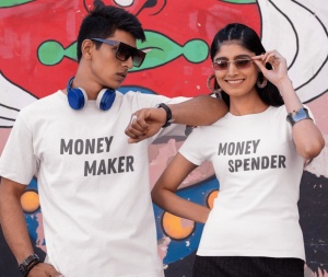 Un bărbat și o femeie purtând tricouri albe, bărbatul cu textul 'Money Maker' și femeia cu textul 'Money Spender', pozând cu atitudine în fața unui perete colorat, cu detalii artistice.