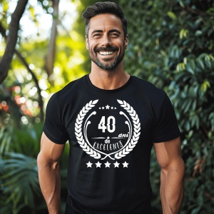 Un bărbat zâmbitor purtând un tricou negru cu textul ''40 de ani de excelență'', înconjurat de o coroană de lauri.