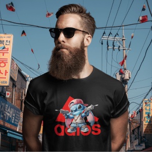 Bărbat cu barbă și ochelari de soare, purtând un tricou negru cu un design ce include un personaj animat albastru(Stitch) stil streetwear ținând două arme de jucărie, în fața unui fundal urban cu semne în limba coreeană și logo stilizat Adidas în roșu.