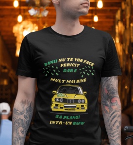 Un bărbat poartă un tricou negru cu un mesaj amuzant în limba română care spune 'Banii nu te vor face fericit, dar e mult mai bine să plângi într-un BMW', însoțit de o ilustrație a unei mașini BMW galbene. Fundalul este iluminat cald, sugerând un interior