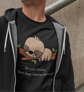 Un bărbat poartă un tricou negru cu o ilustrație drăguță a unui leneș care doarme pe o creangă. Sub imagine este textul 'Nu sunt leneș, Sunt doar foarte relaxat'. Bărbatul poartă o jachetă gri cu fermoar, iar fundalul este un perete din beton.