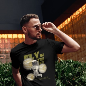 Un bărbat poartă ochelari de soare și un tricou negru cu mesajul 'Fly in the Sky', ilustrat cu un astronaut și imagini stilizate ale planetelor. Bărbatul își ajustează ochelarii într-un mediu urban cu lumini portocalii reflectate în fundal.
