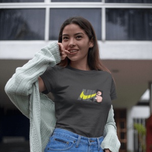 Femeie purtând un tricou negru cu un design grafic ce include textul 'NIKE' și un personaj stilizat(Catwoman), având pe umeri un cardigan deschis și pozând afară, zâmbind ușor.