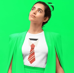Fată purtând un tricou alb cu un design grafic stilizat de cravată și guler de cămașă, completat cu un sacou verde deschis, pe un fundal verde vibrant, uitându-se în sus.