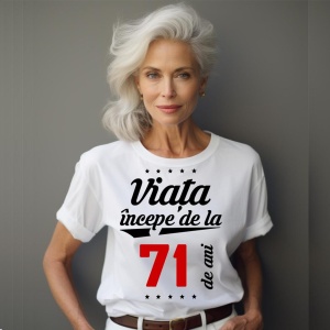 O femeie purtând un tricou alb cu textul  'Viața începe de la 71 de ani'. Fundal din lemn cu diferite nuanțe de maro și verde.