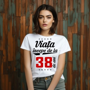 O femeie purtând un tricou alb cu textul  'Viața începe de la 38 de ani'. Fundal din lemn cu diferite nuanțe de maro și verde.