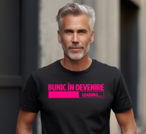 Bărbat purtând un tricou negru cu mesajul în română: 'Bunic în devenire. Loading...' cu un indicator de progres roz, fotografiat într-un decor urban.