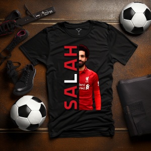 Tricou negru personalizat cu imaginea fotbalistului Salah și text vertical roșu cu numele 'Salah', așezat pe o masă cu accesorii de fotbal, inclusiv mingi și ghete.