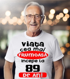 Un bărbat purtând un tricou alb cu textul ''Viața cea mai frumoasă începe la 89 de ani''.