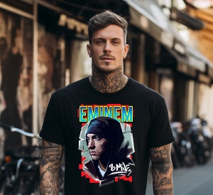 Un bărbat tatuat, purtând un tricou negru imprimat cu un portret artistic al lui Eminem și textul "Eminem" în culori vibrante. În fundal, se văd biciclete și o stradă urbană cu magazine.