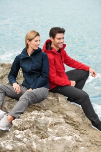 Femeie si barbat stand pe marginea unei stanci imbracati in jachete softshell de culoare rosu si albastru