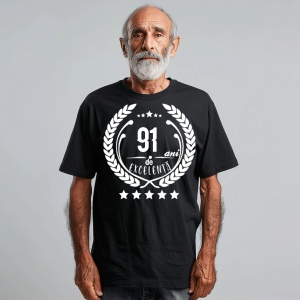 Un bărbat zâmbitor purtând un tricou negru cu textul ''91 de ani de excelență'', înconjurat de o coroană de lauri.