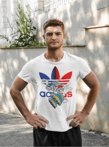 Bărbat purtând un tricou alb cu un design colorat ce include un personaj animat și un logo reinterpretat în culori roșu și albastru, pozând într-un cadru exterior, lângă un zid alb cu plante.