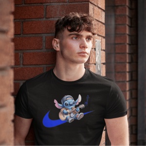 Tânăr purtând un tricou negru cu un personaj animat albastru(Stitch) cântând la chitară, situat deasupra unui logo stilizat albastru, stând lângă un zid de cărămidă roșie.