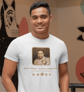 Un bărbat zâmbitor poartă un tricou alb cu un design inspirat de un player muzical, prezentând o fotografie a cântărețului Florin Salam și titlul piesei '10 Ani de Ghinion să Ai' scris dedesubt.