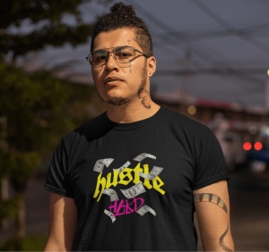 Bărbat cu tatuaje pe față și gât, purtând un tricou negru cu textul 'hustle HARD' și imagini cu bancnote, pe un fundal urban la apus sau în lumina de seară. Poartă ochelari și are o expresie serioasă.