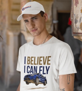 Bărbat purtând un tricou alb cu designul unei mașini sport albastre în zbor și textul 'I BELIEVE I CAN FLY' în albastru și auriu, alături de o șapcă neagră inscripționată cu logo-ul 'Imbracaminte Simplă', pozând într-un cadru urban.