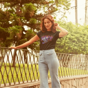Fată stând lângă o balustradă, purtând un tricou negru cu un design grafic viu(personajul Stitch) și pantaloni evazați, într-un cadru verde și natural.