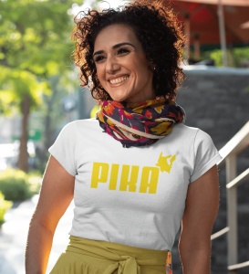 Femeie zâmbitoare purtând un tricou alb cu design galben ce include textul 'PIKA' și o siluetă stilizată a unui personaj în colțul din dreapta al textului. Ea poartă un fular colorat și o fustă galbenă, iar fundalul arată o stradă cu verdeață, creând o at