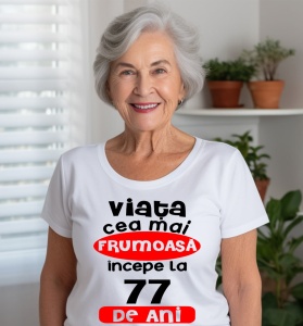 Femeie care poartă un tricou alb personalizat cu mesajul: ''Viata cea mai frumoasa incepe la 77 de ani''.