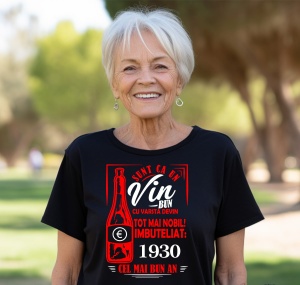 Femeie zâmbitoare purtând un tricou negru cu un mesaj în română despre vin, în care se menționează că este ca un vin bun care devine mai nobil cu vârsta, îmbuteliat în 1930, cel mai bun an.