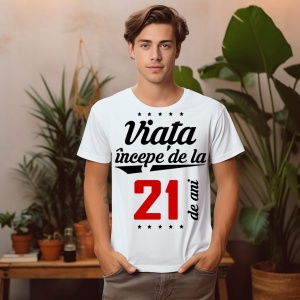 Tânăr purtând un tricou alb cu mesajul 'Viața începe de la 21 de ani', stând într-o cameră decorată cu plante.