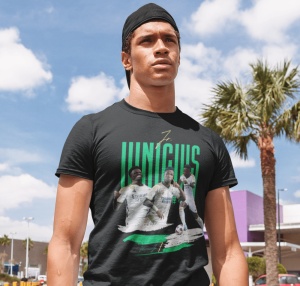 Un tânăr purtând o șapcă întoarsă poartă un tricou negru cu design grafic dedicat jucătorului de fotbal Vinícius, cu imagini ale acestuia în diferite ipostaze și numele său scris cu litere verzi. Fundalul arată un cer senin și un palmier.