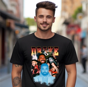 Un bărbat zâmbitor purtând un tricou negru cu un design ce include imagini multiple ale artistului Drake, cu numele 'Drake' afișat deasupra în font stilizat, pozând într-un mediu urban.