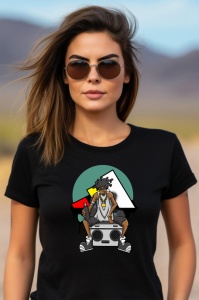 Femeie purtând ochelari de soare și un tricou negru cu un design stilizat, înfățișând un personaj cu păr afro, lănțișor și pantaloni scurți, stând pe o boxă, având un fundal geometric în culori verde, negru, roșu și galben.