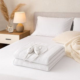 Сгънато бяло електрическо одеяло с два контролера върху легло в модерна спалня