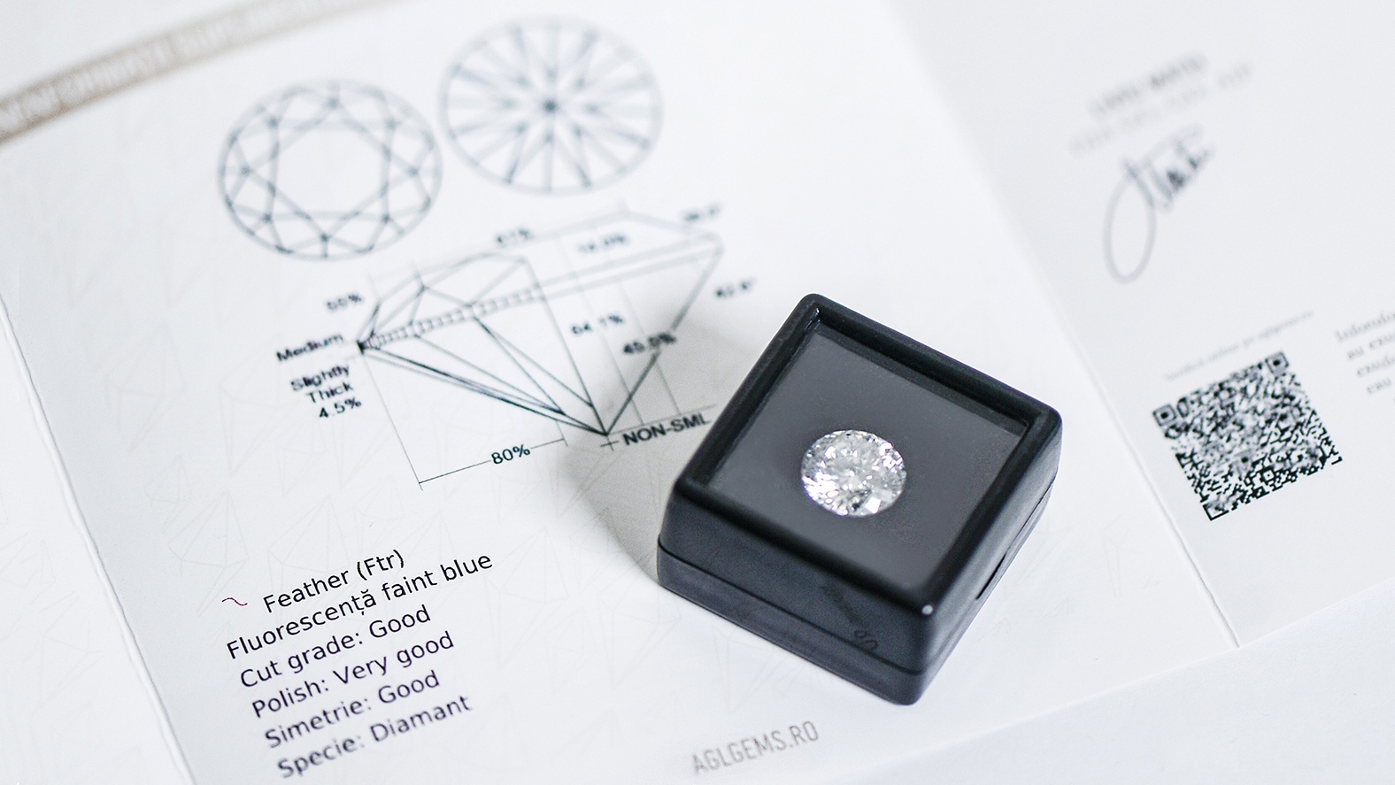 Diamant prezentat in cutie alaturi de certificatul gemologic AGL (detalii vizibile: Cut Grade, Polish, Symmetry) emis conform standardelor GIA ca parte a procesului de evaluare diamante